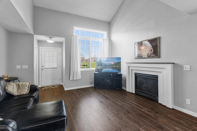 living area featuring wood finished floors, baseboards, vaulted ceiling, a glass covered fireplace, and a textured ceiling