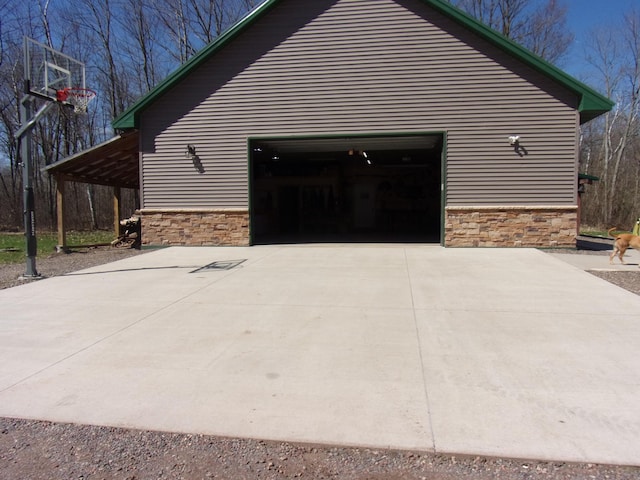 view of side of property featuring concrete driveway, stone siding, and a garage