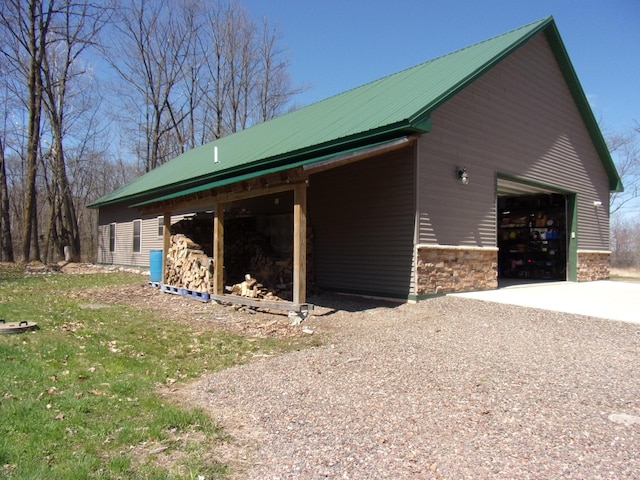 view of property exterior with a garage, driveway, metal roof, and stone siding
