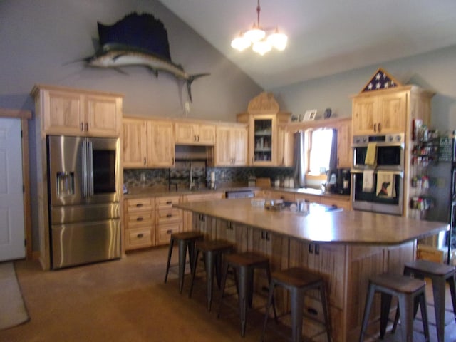 kitchen with light brown cabinetry, appliances with stainless steel finishes, a kitchen breakfast bar, and vaulted ceiling