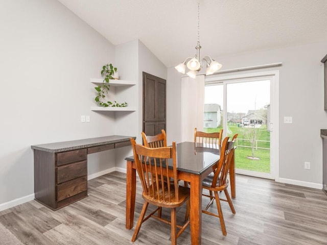 dining space with light wood finished floors, an inviting chandelier, built in desk, baseboards, and vaulted ceiling