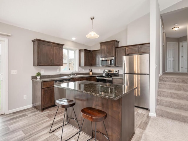 kitchen with light wood finished floors, dark brown cabinets, dark stone counters, stainless steel appliances, and baseboards