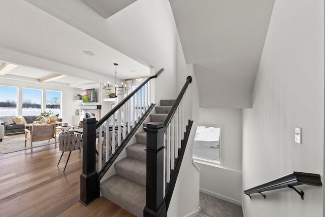 4181 Arbor Dr, Woodbury, MN 55129 - stairs featuring wood finished floors, beam ceiling, a stone fireplace, baseboards, and a notable chandelier