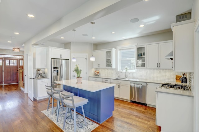 kitchen with light wood finished floors, decorative backsplash, wall chimney exhaust hood, appliances with stainless steel finishes, and a kitchen island