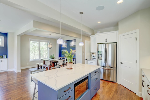 kitchen featuring built in microwave, a breakfast bar, stainless steel refrigerator with ice dispenser, white cabinets, and light wood-type flooring
