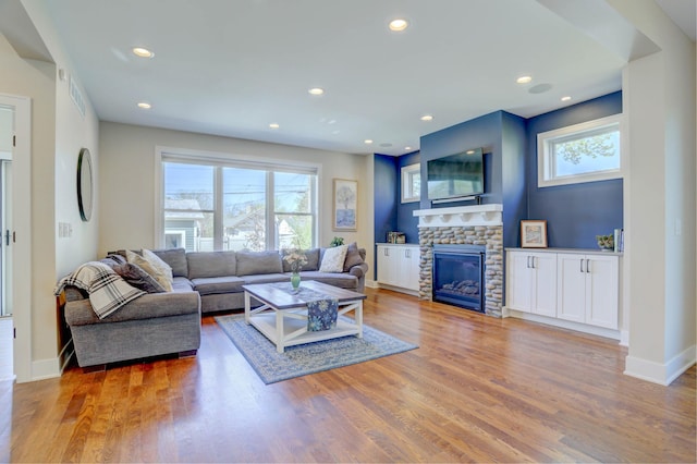 living room featuring a fireplace, baseboards, light wood-type flooring, and recessed lighting