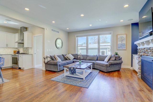 living area featuring recessed lighting, baseboards, a stone fireplace, visible vents, and wood finished floors