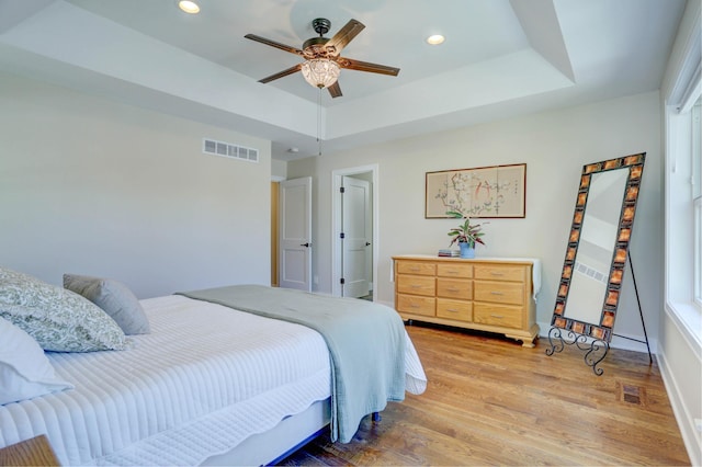 bedroom with a tray ceiling, recessed lighting, light wood-style flooring, and visible vents