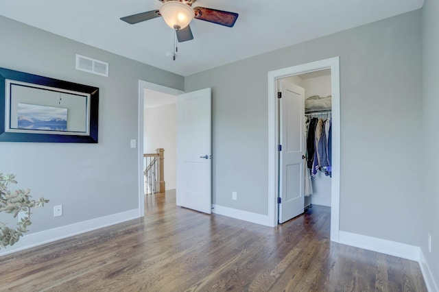 unfurnished bedroom featuring wood finished floors, a walk in closet, visible vents, baseboards, and ceiling fan