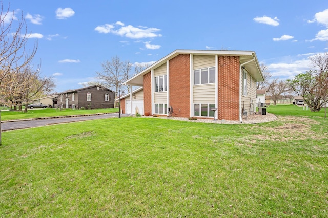 exterior space featuring a lawn, brick siding, driveway, and central AC unit