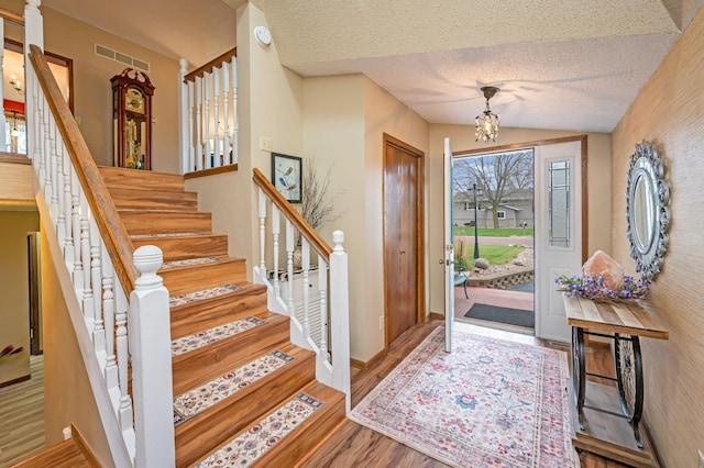 foyer entrance with a notable chandelier, stairs, wood finished floors, vaulted ceiling, and visible vents