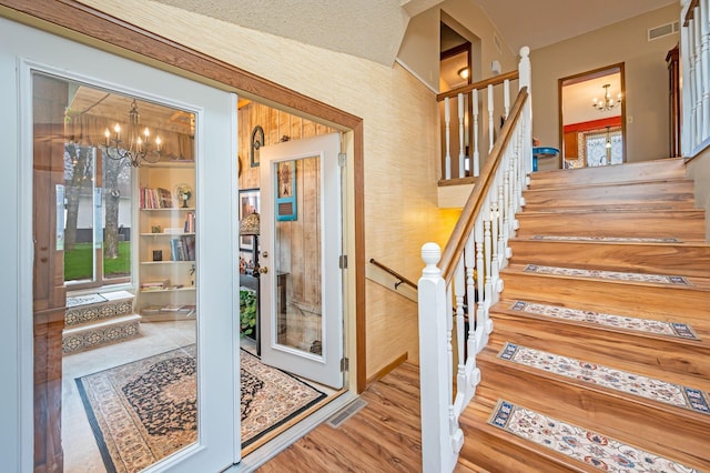 staircase featuring visible vents, wood finished floors, and a notable chandelier