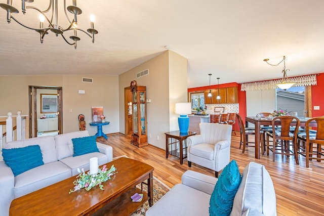 living area with visible vents, light wood finished floors, baseboards, and an inviting chandelier