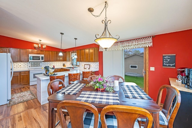 dining room with a notable chandelier, lofted ceiling, and light wood finished floors
