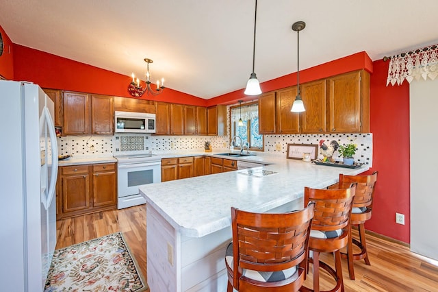 kitchen with a peninsula, light wood finished floors, vaulted ceiling, and white appliances