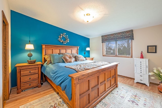 bedroom with baseboards, vaulted ceiling, light wood finished floors, and a textured ceiling