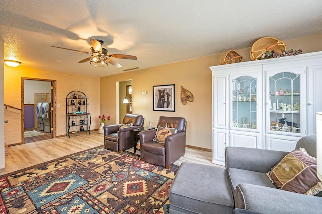 living area featuring independent washer and dryer, ceiling fan, baseboards, light wood-type flooring, and visible vents