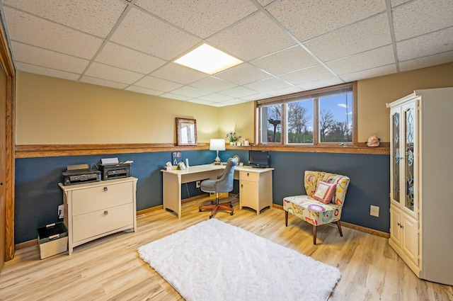 office area with baseboards, light wood finished floors, and a drop ceiling
