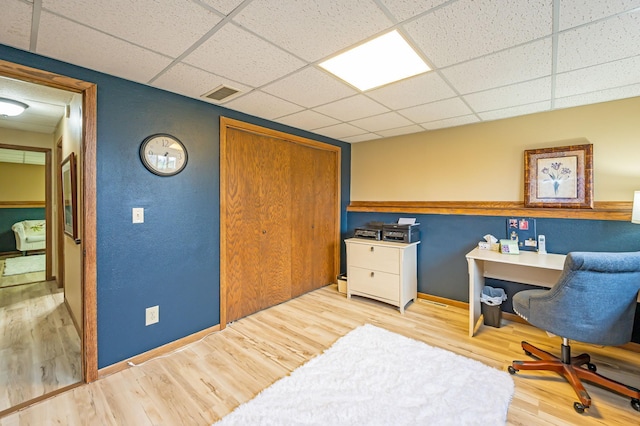 office space featuring baseboards, visible vents, a paneled ceiling, and wood finished floors