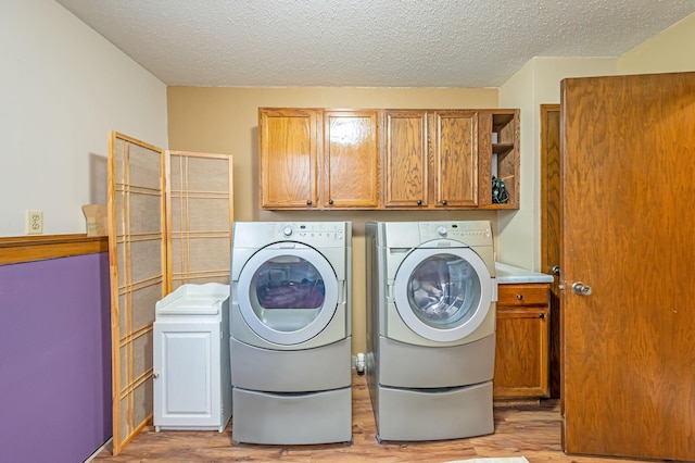 washroom with light wood-style floors, separate washer and dryer, a textured ceiling, and cabinet space