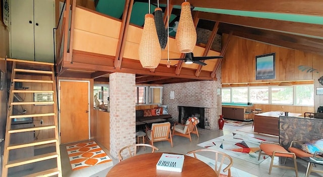 tiled living area featuring ceiling fan, a brick fireplace, wooden walls, vaulted ceiling with beams, and ornate columns