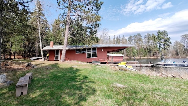 back of property with a lawn, a chimney, a water view, and metal roof