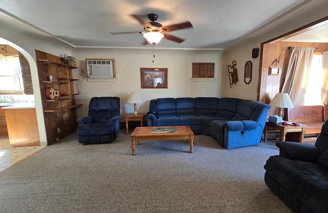 living area featuring carpet floors, a wall unit AC, a ceiling fan, arched walkways, and crown molding