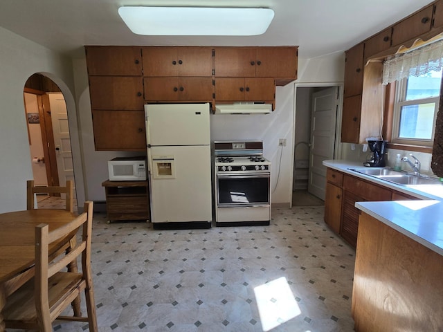 kitchen featuring a sink, white appliances, light floors, under cabinet range hood, and arched walkways