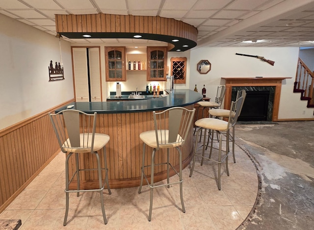 bar featuring indoor wet bar, a wainscoted wall, light tile patterned floors, a paneled ceiling, and a premium fireplace