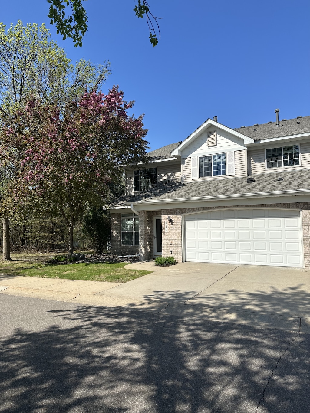 traditional home featuring an attached garage, roof with shingles, brick siding, and concrete driveway