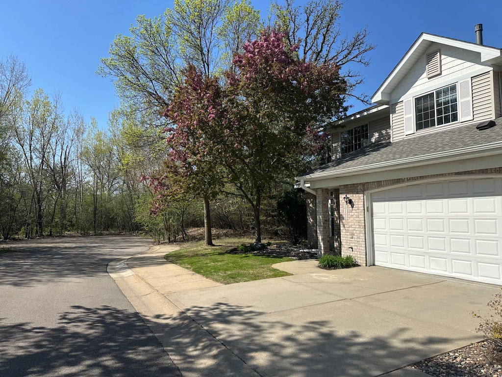 view of side of property with brick siding, a shingled roof, and concrete driveway