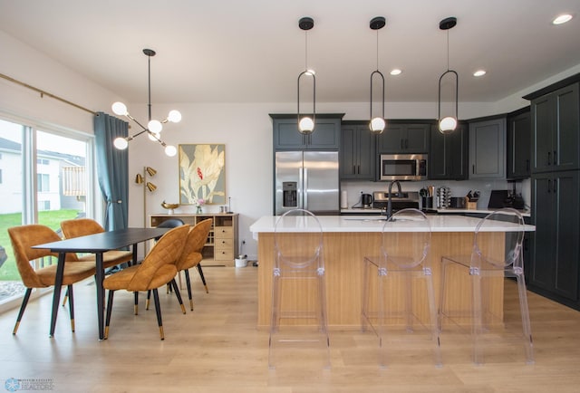4964 Big Goose Ln S, Fargo, ND 58104 - kitchen with stainless steel appliances, light countertops, light wood-style flooring, a center island with sink, and decorative light fixtures