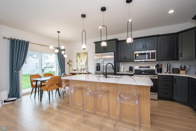 4964 Big Goose Ln S, Fargo, ND 58104 - kitchen with appliances with stainless steel finishes, a sink, a kitchen island with sink, light wood-type flooring, and light countertops