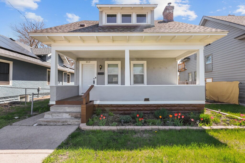 bungalow-style house featuring covered porch, a chimney, fence, and stucco siding