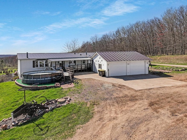 view of front of property featuring an outdoor pool, metal roof, a front yard, and a detached garage
