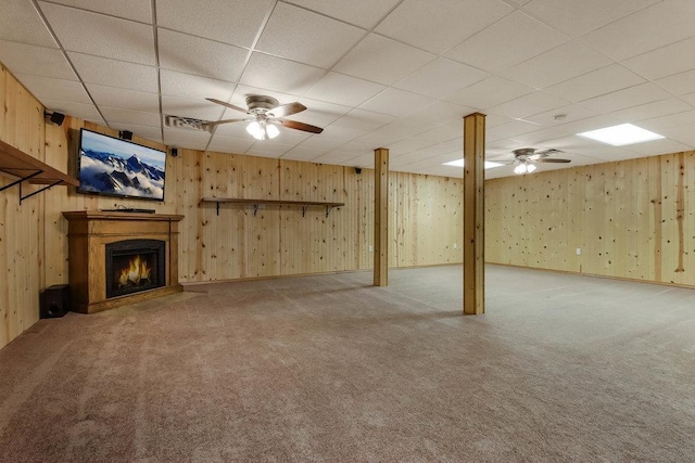 finished basement featuring carpet flooring, a ceiling fan, a lit fireplace, and a paneled ceiling