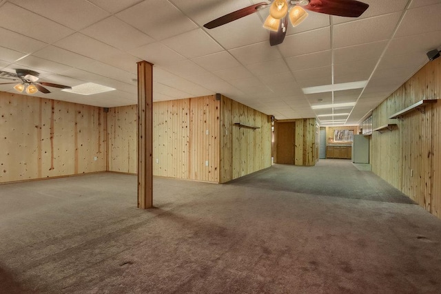 finished below grade area featuring carpet floors, a ceiling fan, a paneled ceiling, and wooden walls