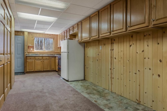 kitchen featuring freestanding refrigerator, light carpet, a drop ceiling, wooden walls, and stainless steel electric range oven