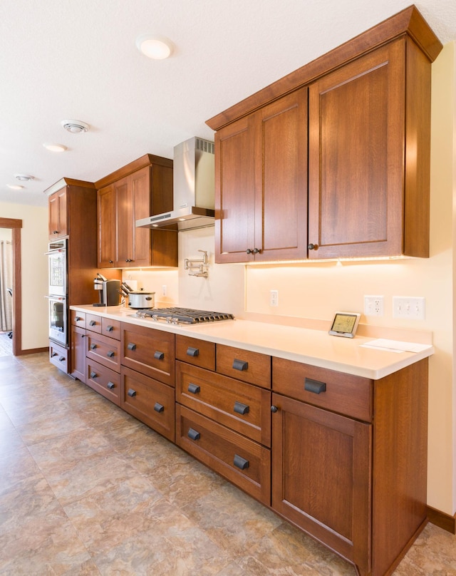 kitchen with wall chimney exhaust hood, stainless steel appliances, brown cabinetry, light countertops, and baseboards