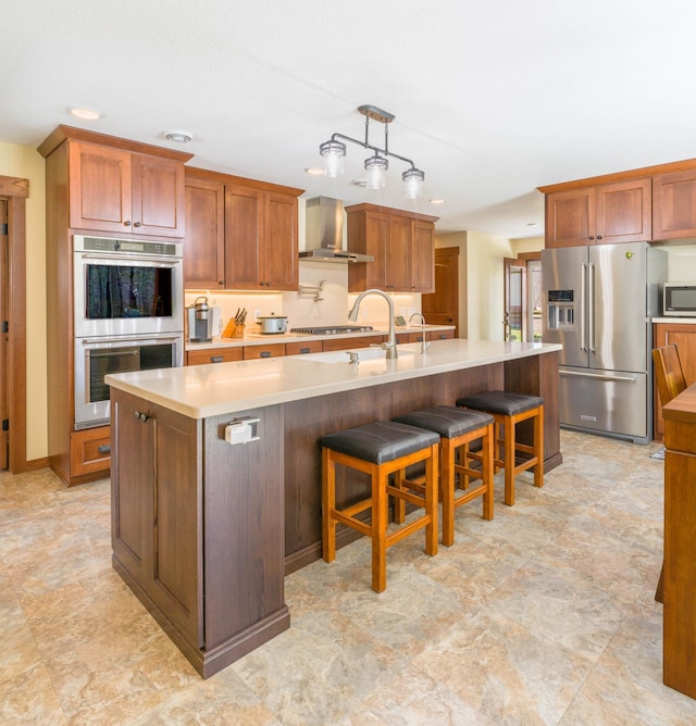 kitchen featuring stainless steel appliances, wall chimney exhaust hood, light countertops, a large island, and a sink