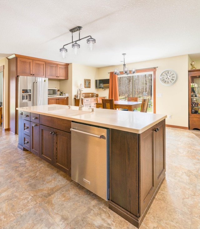 kitchen with appliances with stainless steel finishes, a sink, a center island with sink, light countertops, and hanging light fixtures