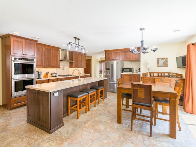 kitchen featuring appliances with stainless steel finishes, a chandelier, light countertops, wall chimney range hood, and hanging light fixtures