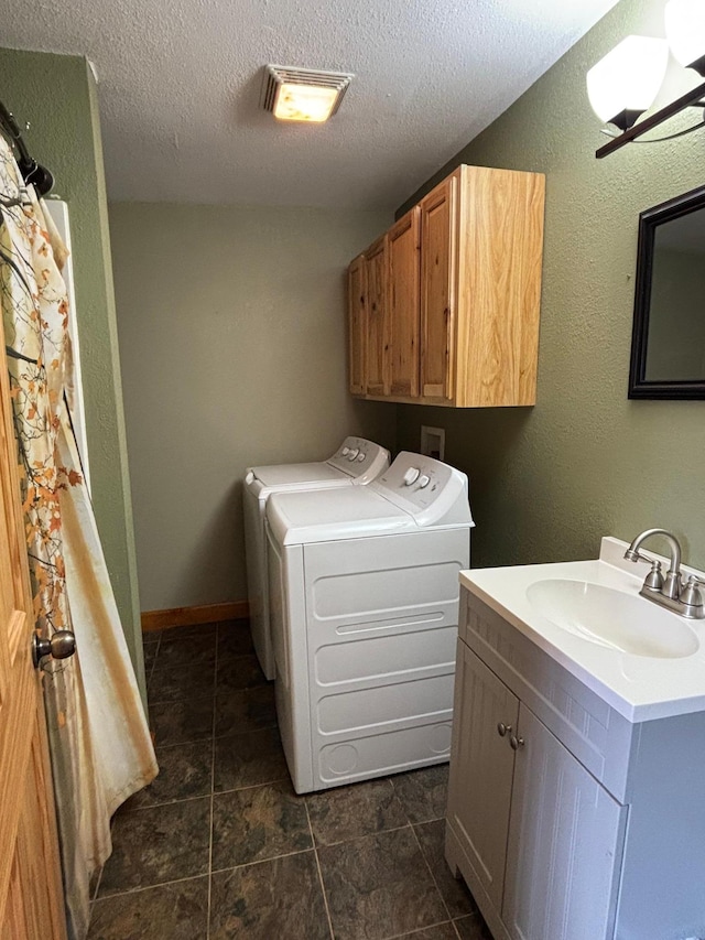 laundry room featuring washing machine and dryer, a sink, cabinet space, a textured ceiling, and visible vents