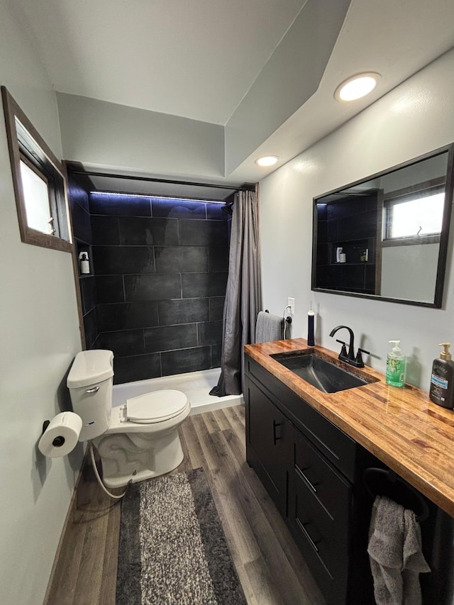 full bathroom featuring toilet, wood finished floors, tiled shower, vanity, and recessed lighting