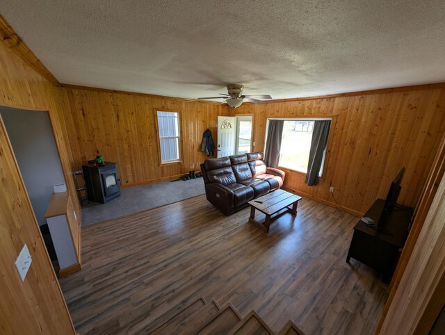 living room featuring a textured ceiling, a wood stove, wood walls, wood finished floors, and a ceiling fan