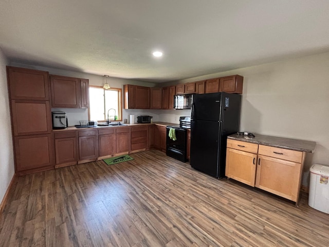 kitchen with black appliances, wood finished floors, a sink, and baseboards