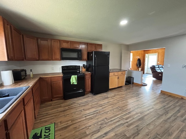 kitchen with black appliances, light wood-type flooring, a sink, recessed lighting, and brown cabinetry