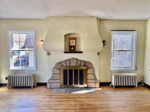 interior space with radiator heating unit, a textured ceiling, a fireplace, and wood finished floors