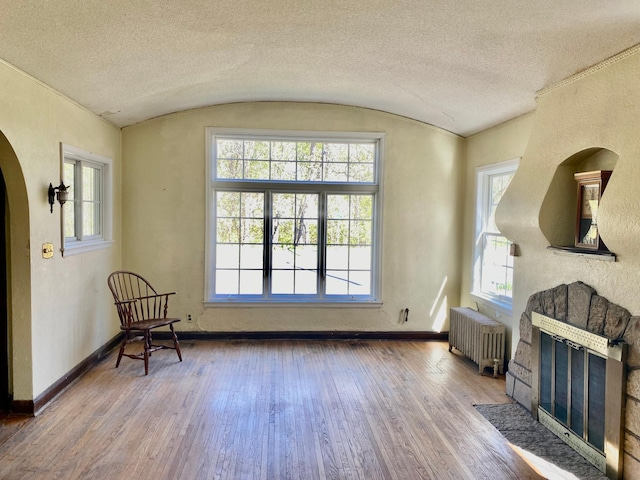 sitting room with wood-type flooring, arched walkways, a textured ceiling, and radiator