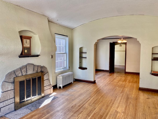 unfurnished living room with wood-type flooring, arched walkways, radiator heating unit, baseboards, and lofted ceiling